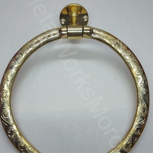 K&ouml;nnte beinhalten: Ein runder, dekorativer Handtuchring in Goldton mit einem komplizierten, gravierten Blumenmuster. Der Ring ist an einer Wandhalterung mit zwei Schrauben befestigt.