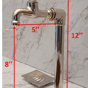 K&ouml;nnte beinhalten: Ein polierter Chrom-Wasserhahn mit einem kreuzf&ouml;rmigen Griff, montiert auf einem Chromrohr. Der Wasserhahn ist 5 Zoll hoch und das Rohr 12 Zoll hoch. Der Wasserhahn ist auf einer Arbeitsplatte mit einem Seifenspender und einem gro&szlig;en, goldfarbenen Waschbecken montiert.