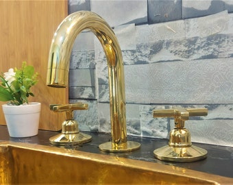 May include: A gold-toned bathroom faucet with two handles and a high spout. The faucet is mounted on a black countertop.