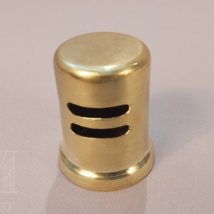 May include: A gold-colored metal vent cover with two horizontal slots. The vent cover is cylindrical and has a smooth, polished finish.