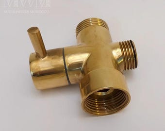 May include: A gold-colored brass shower diverter valve with a lever handle. The valve has three connections, one on each side and one on the bottom.