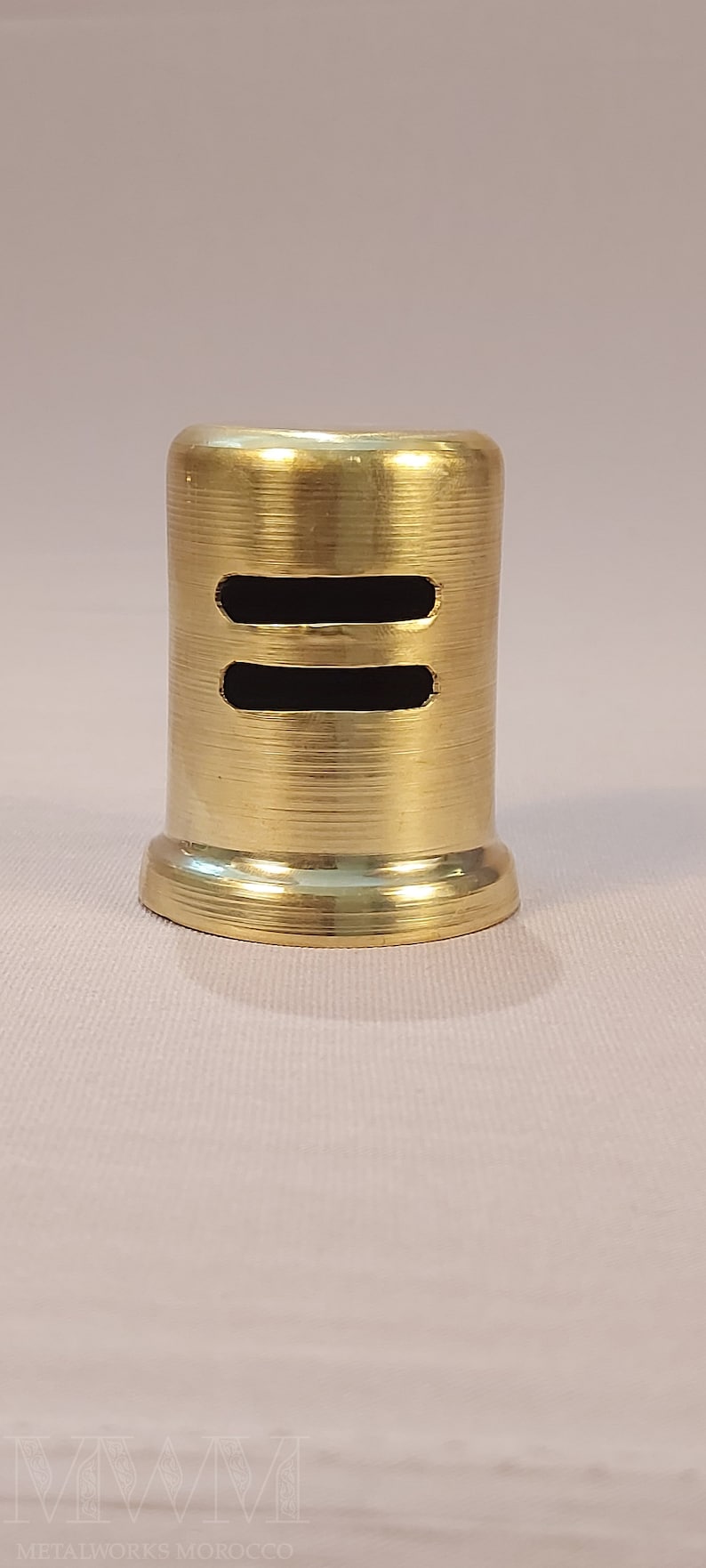May include: A gold metal bottle stopper with two horizontal slits. The stopper has a smooth, shiny finish.