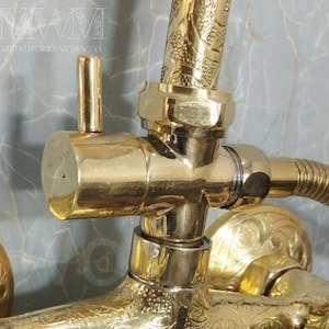 Puede incluir: Grifo de ducha dorado con intrincados dise&ntilde;os florales. El grifo tiene una palanca y una alcachofa de ducha con un patr&oacute;n decorativo. El grifo est&aacute; conectado a una tuber&iacute;a con una manguera.