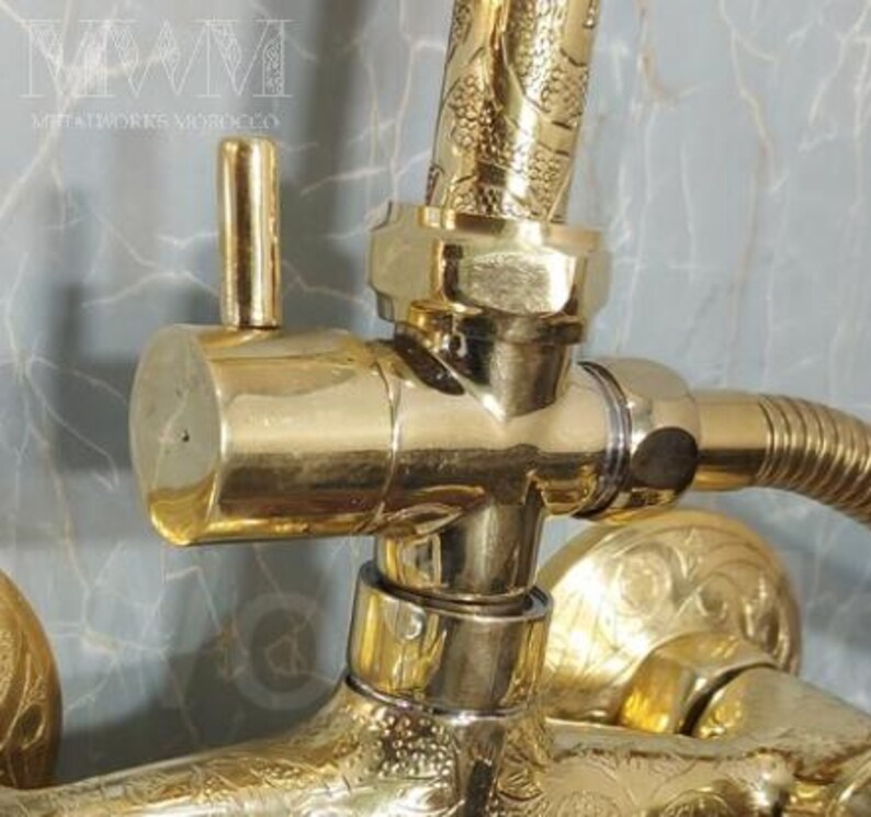 Puede incluir: Grifo de ducha dorado con intrincados dise&ntilde;os florales. El grifo tiene una palanca y una alcachofa de ducha con un patr&oacute;n decorativo. El grifo est&aacute; conectado a una tuber&iacute;a con una manguera.