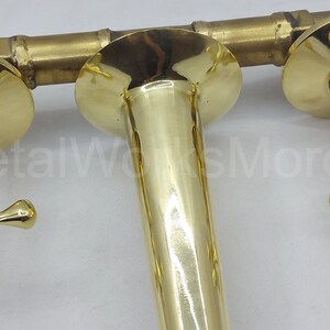 May include: A gold-toned faucet with two cross-shaped handles and a central spout. The faucet is wall-mounted and has a polished finish.