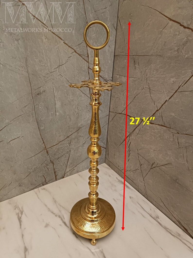 May include: Gold metal umbrella stand with a round top and a decorative base. The stand is 27 1/2 inches tall.
