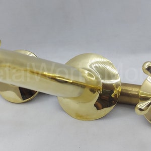 May include: A gold-toned brass faucet with two cross-shaped handles. The faucet has a curved spout and is designed for wall mounting.