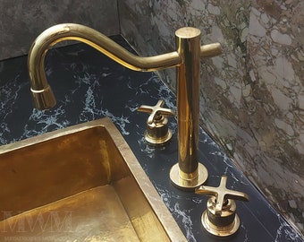 May include: Gold-toned faucet with a curved spout and two cross-shaped handles. The faucet is mounted on a black marble countertop with a gold-toned sink.