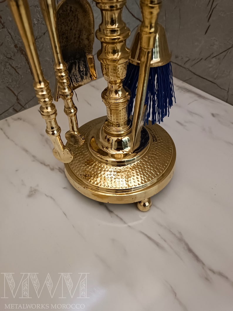 May include: A gold metal fireplace tool set with a brush, shovel, and poker. The tools are mounted on a decorative stand with a hammered finish.