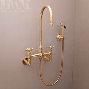 Könnte beinhalten: Ein goldfarbenes Badezimmer-Armaturenset mit hohem Auslauf und Kreuzgriffventilen. Enthält einen passenden Hand-Bidet-Sprayer. Der Text "METALWORKS MOROCCO" ist oben sichtbar.