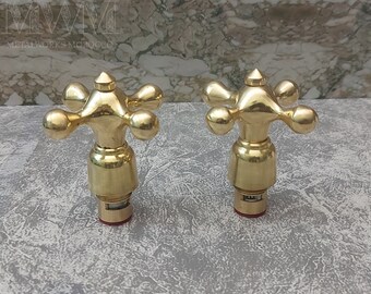 Peut inclure: Deux poignées de robinet dorées avec un design en forme de croix et un sommet pointu. Les poignées ont une base ronde et sont en métal.