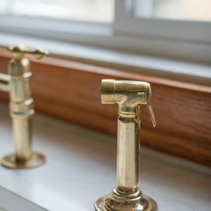May include: A close-up of a gold-toned faucet with a lever handle and a spout. The faucet is mounted on a white countertop.