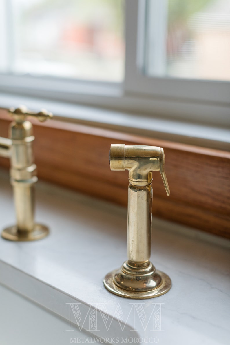 May include: A close-up of a gold-toned faucet with a lever handle and a spout. The faucet is mounted on a white countertop.