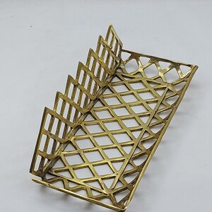 May include: A gold metal napkin holder with a geometric design. The holder has a rectangular base and a series of vertical dividers that create a fan-like shape.