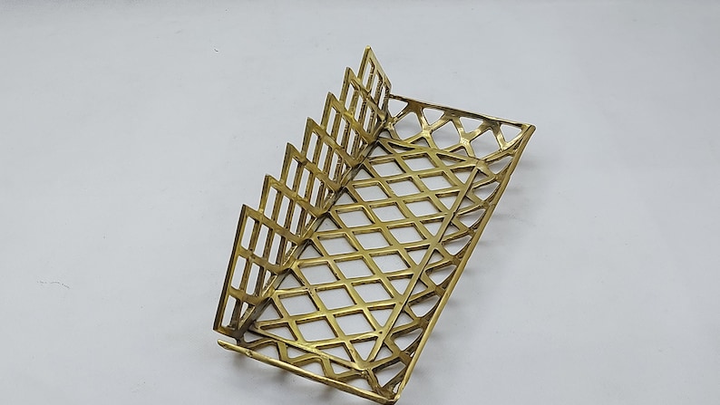 May include: A gold metal napkin holder with a geometric design. The holder has a rectangular base and a series of vertical dividers that create a fan-like shape.