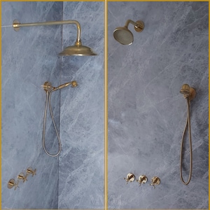 May include: Two gold shower heads with a handheld shower head and a fixed shower head. The shower heads are mounted on a gray tiled wall. There are three gold shower knobs on the wall.