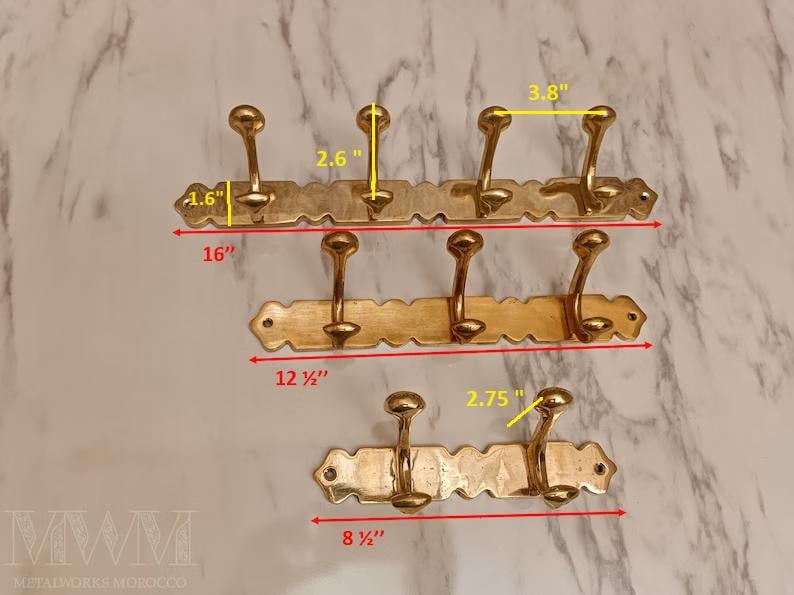 May include: Three brass coat racks of varying sizes. The largest is 16 inches wide with three hooks, the medium is 12.5 inches wide with three hooks, and the smallest is 8.5 inches wide with two hooks. Each hook is approximately 2.6 inches tall.