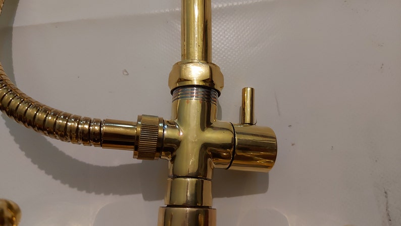 Puede incluir: Primer plano de un grifo dorado con una manguera y una v&aacute;lvula desviadora. El grifo tiene un acabado pulido y un dise&ntilde;o sencillo.