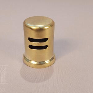May include: A gold-colored metal vent cover with two horizontal slots. The vent cover is cylindrical in shape.