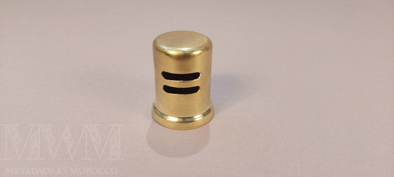 May include: A gold-colored metal vent cover with two horizontal slots. The vent cover is cylindrical in shape.