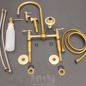 May include: A gold-toned bathroom faucet set with two handles, a spout, a hand shower, and a soap dispenser. The set includes two hoses, two washers, and two decorative plates.