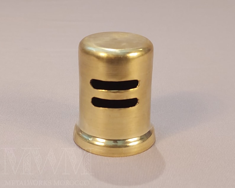 May include: A gold metal vent cover with two rectangular openings. The vent cover is cylindrical in shape.