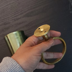 May include: A gold metal towel ring with a round base and a screw hole. The ring is held in a hand.