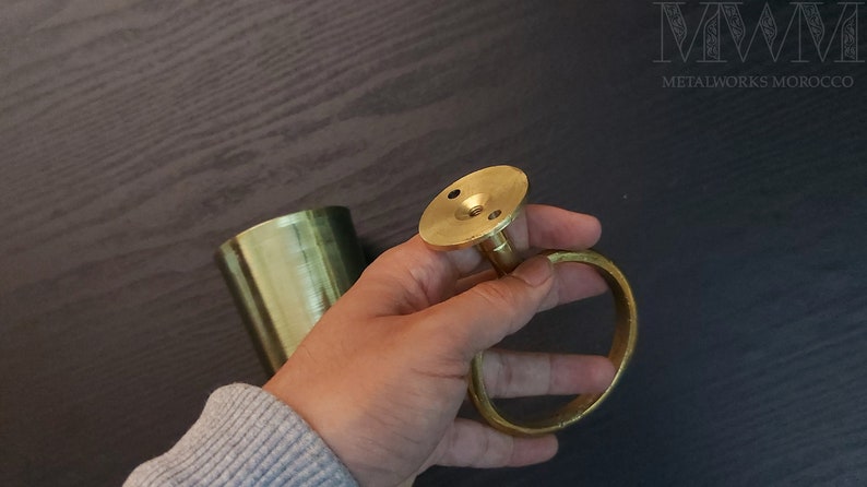 May include: A gold metal towel ring with a round base and a screw hole. The ring is held in a hand.