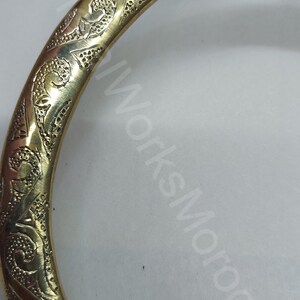 K&ouml;nnte beinhalten: Ein goldfarbener Handtuchring aus Metall mit einem komplizierten, gravierten Blumendesign.