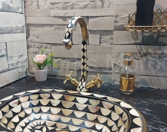 May include: A black and white oval sink with a decorative pattern. The sink is made of mother of pearl and has a gold-toned faucet.