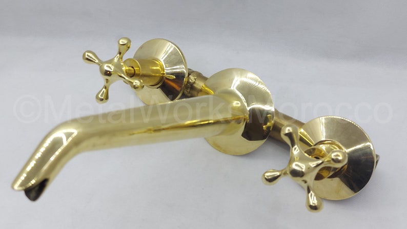 May include: A polished brass faucet with two cross-shaped handles and a curved spout.