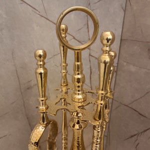 May include: A gold metal fireplace tool set with a round top and three tools. The tools have a hammered finish and are attached to a decorative stand.