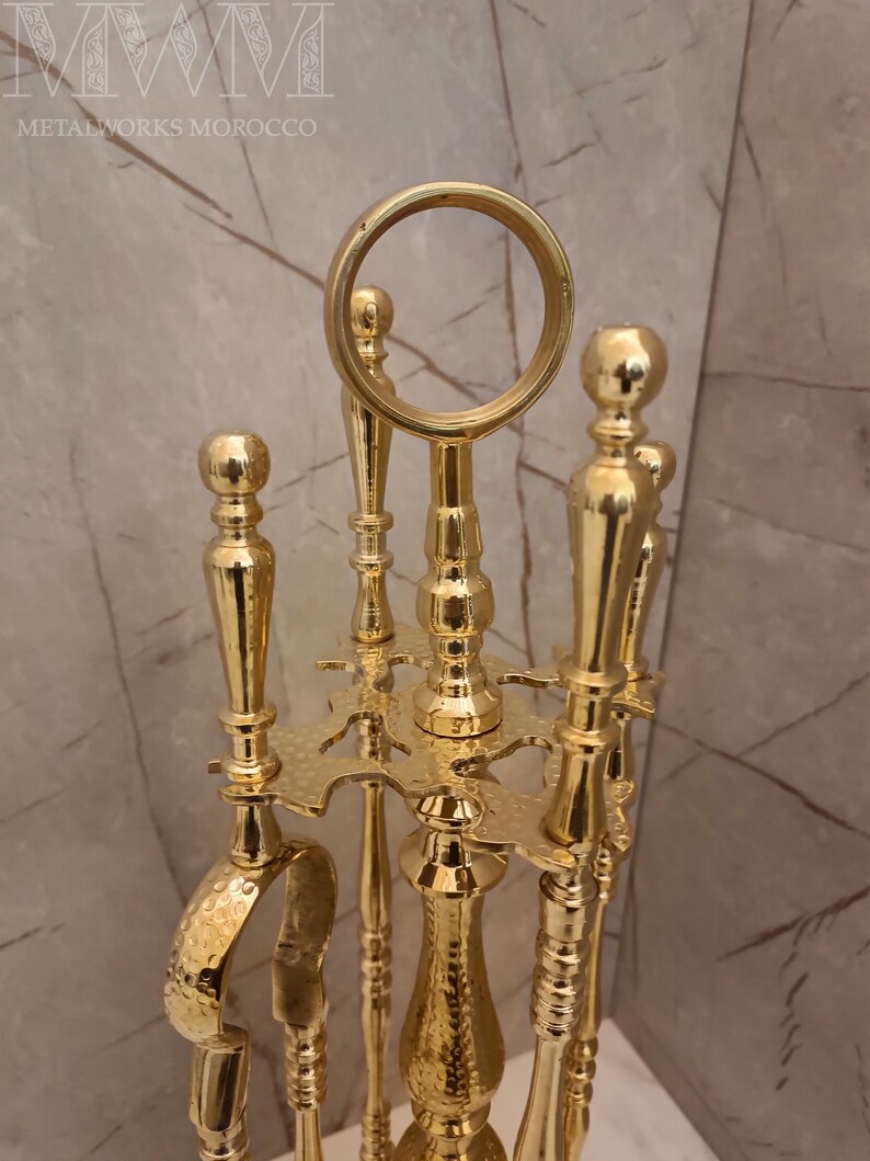 May include: A gold metal fireplace tool set with a round top and three tools. The tools have a hammered finish and are attached to a decorative stand.