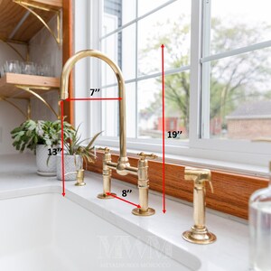 May include: A gold kitchen faucet with a 7-inch tall spout and an 8-inch wide base. The faucet is mounted on a white countertop and has a 19-inch clearance from the countertop to the bottom of the window.