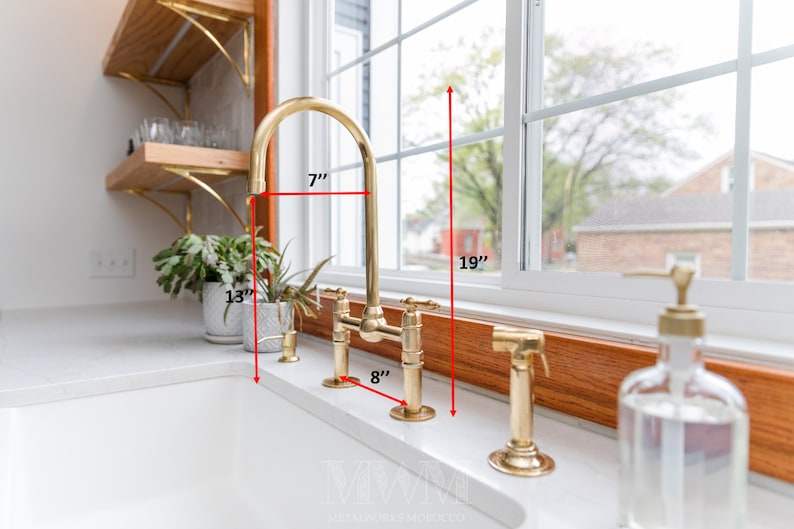 May include: A gold kitchen faucet with a 7-inch tall spout and an 8-inch wide base. The faucet is mounted on a white countertop and has a 19-inch clearance from the countertop to the bottom of the window.