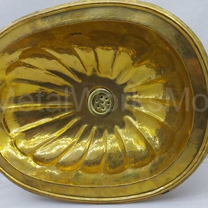 May include: A gold oval-shaped brass sink with a decorative, fluted design. The sink has a round drain in the center.