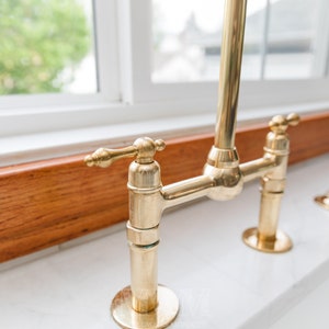 May include: A gold-toned kitchen faucet with a single lever handle and a high spout. The faucet is mounted on a wooden countertop.