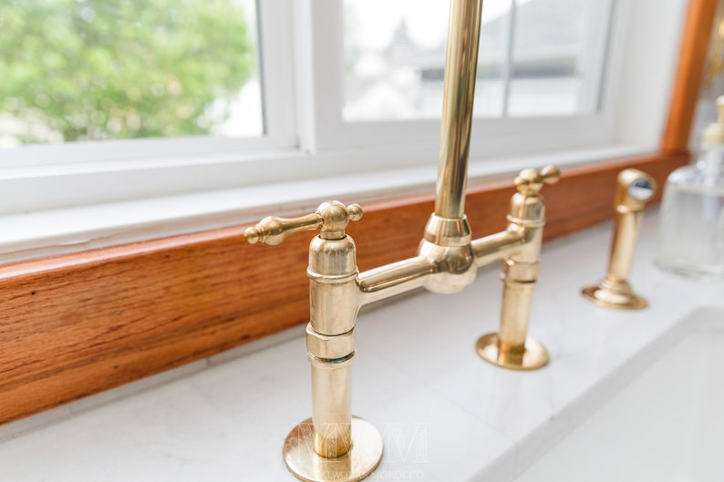 May include: A gold-toned kitchen faucet with a single lever handle and a high spout. The faucet is mounted on a wooden countertop.