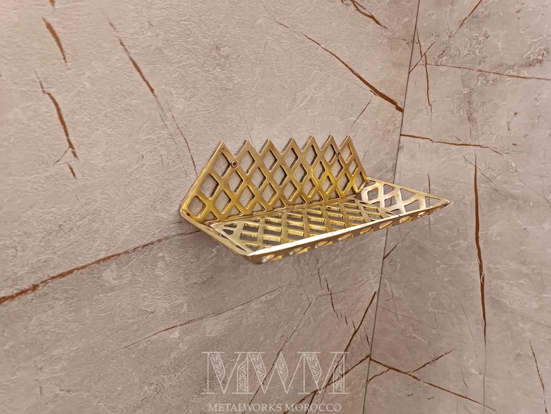 May include: A gold metal shelf with a geometric design. The shelf is mounted on a wall with a light beige background.