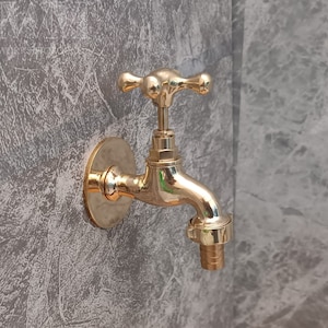 Könnte beinhalten: Ein goldfarbener Metall-Außenwasserhahn mit runder Basis und einem Hebelgriff. Der Wasserhahn hat einen Gewindeanschluss für einen Schlauch.