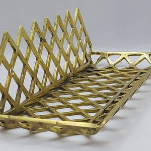 May include: A gold metal tray with a geometric diamond pattern. The tray is open on one side and has a raised edge.