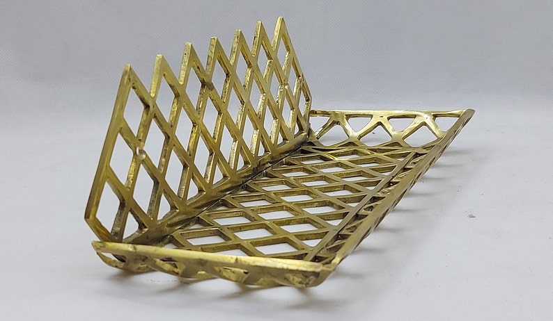 May include: A gold metal tray with a geometric diamond pattern. The tray is open on one side and has a raised edge.