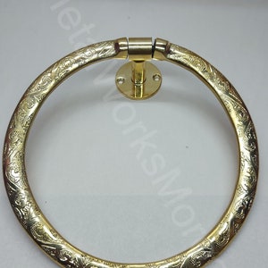 K&ouml;nnte beinhalten: Ein goldfarbener Handtuchring aus Metall mit einem verzierten Design. Der Ring ist an einer Wandhalterung mit einem runden Sockel befestigt.