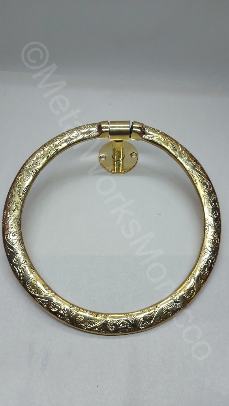K&ouml;nnte beinhalten: Ein goldfarbener Handtuchring aus Metall mit einem verzierten Design. Der Ring ist an einer Wandhalterung mit einem runden Sockel befestigt.