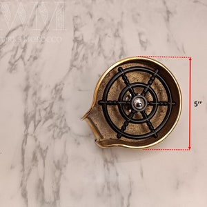 K&ouml;nnte beinhalten: Eine Seifenablage aus Messing mit einem schwarzen Metallrad-Design. Die Ablage ist 12,7 cm hoch.