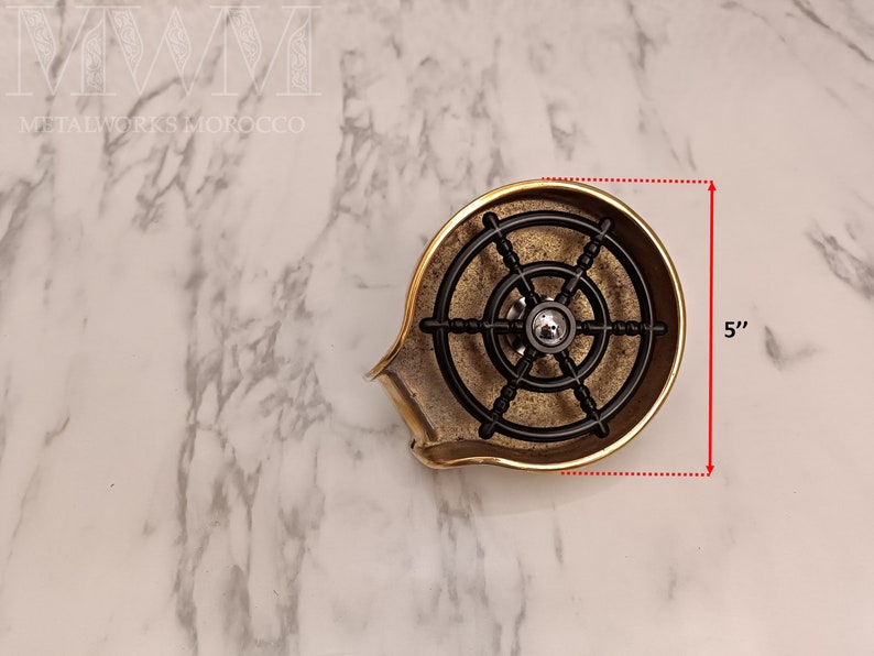 K&ouml;nnte beinhalten: Eine Seifenablage aus Messing mit einem schwarzen Metallrad-Design. Die Ablage ist 12,7 cm hoch.