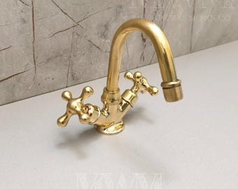 May include: A polished gold-tone brass faucet featuring a high-arched spout and two cross-style handles. The fixture has a reflective metallic finish and a curved design, with a central body connecting the spout to the two side-mounted control knobs.