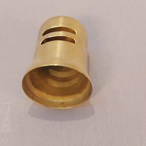 May include: A gold-colored metal cap with two horizontal slits. The cap is designed to fit over a pipe or tube.