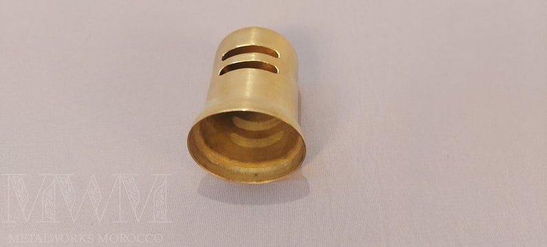 May include: A gold-colored metal cap with two horizontal slits. The cap is designed to fit over a pipe or tube.