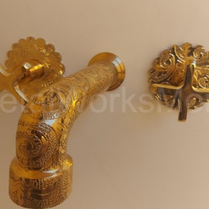 May include: A gold-toned faucet with intricate floral designs. The faucet has two cross-shaped handles with decorative accents.